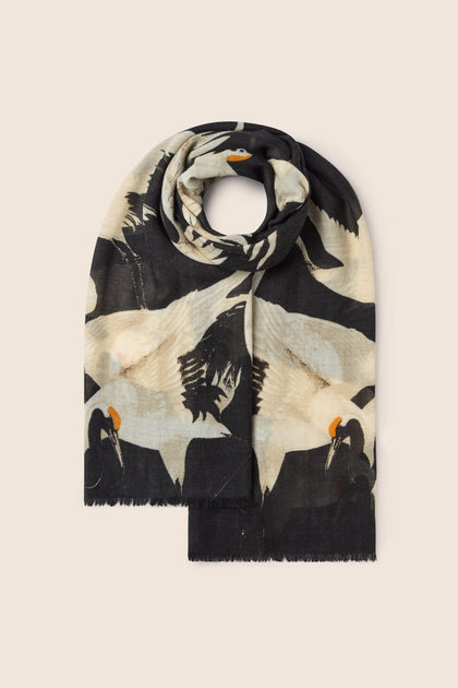 The "Stork Print Woollen Scarf," a vintage-inspired luxury accessory in black and beige, adorned with a pattern of cranes, is neatly folded against a plain background, exuding an Art Deco fashion charm.