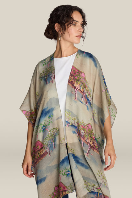 A person wearing the Landscape Wool Throwover with unique prints inspired by Japanese watercolors, featuring scenic trees and buildings. The individual has dark hair pulled back and is looking off to the side.