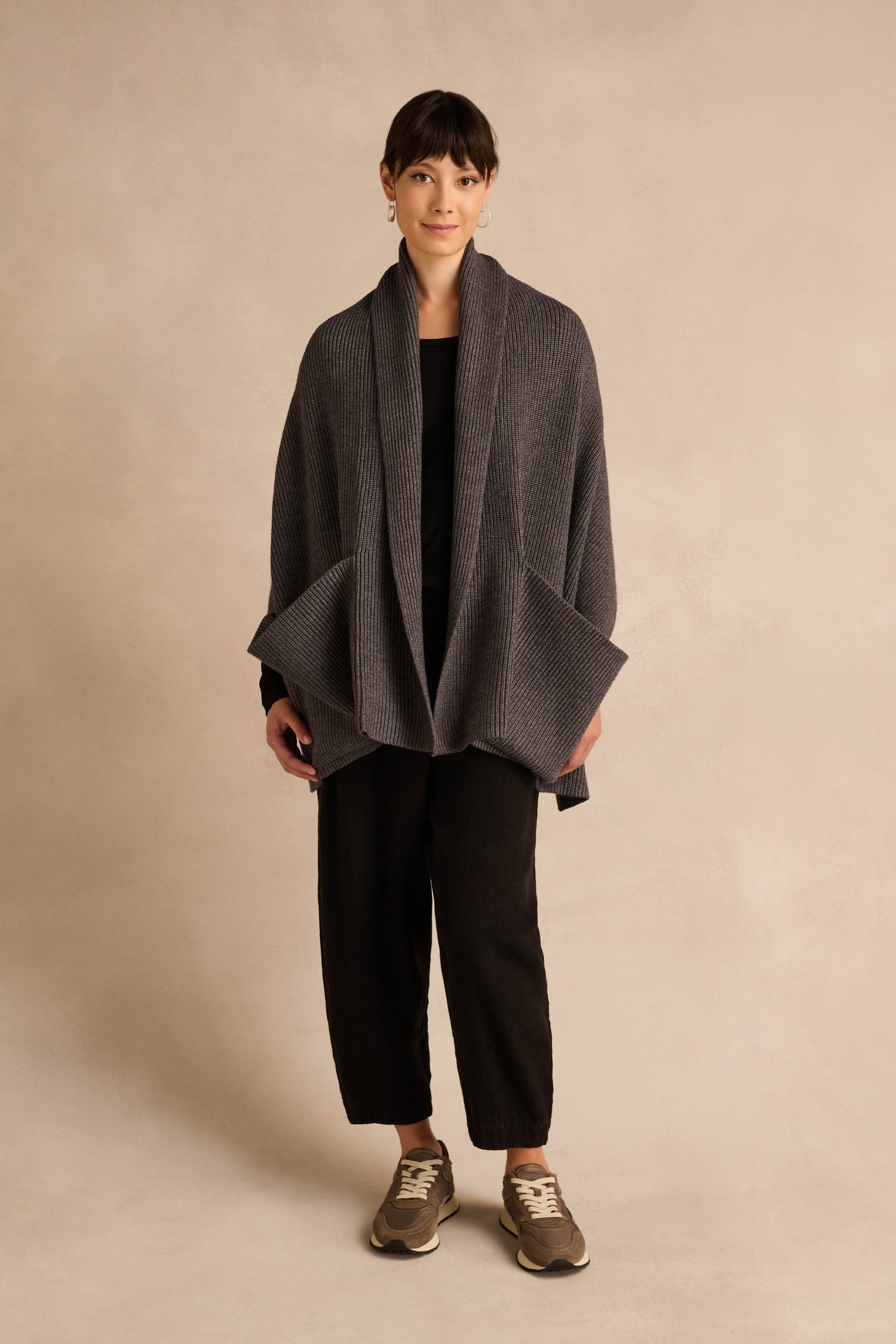 A person stands against a neutral background, wearing the Charcoal Pocket Scarf draped over a black outfit and brown sneakers, with hands relaxed at sides.