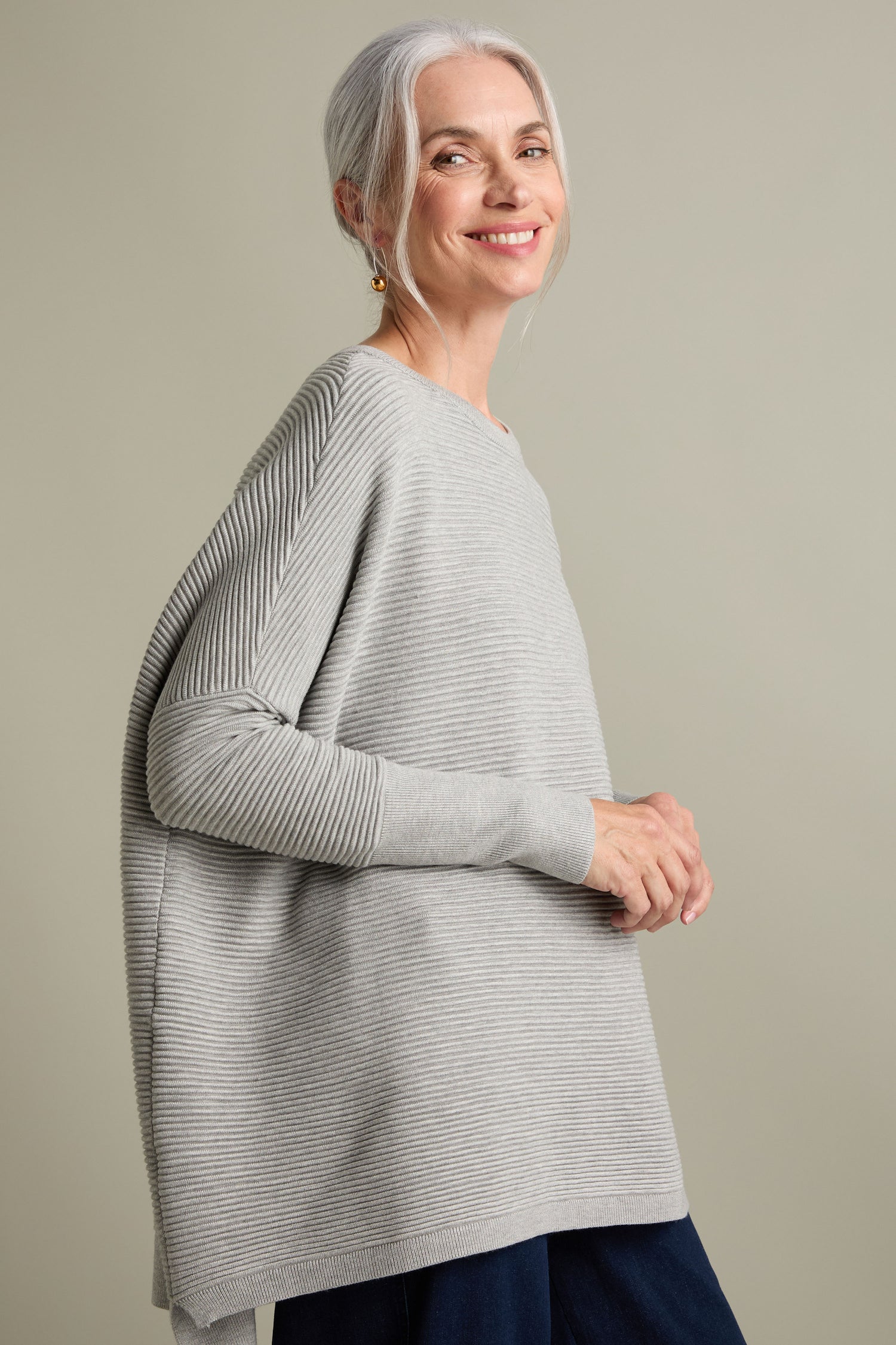 A woman with white hair and a smile wears a Ribbed Jumper in light gray, exuding luxury, against a plain background.