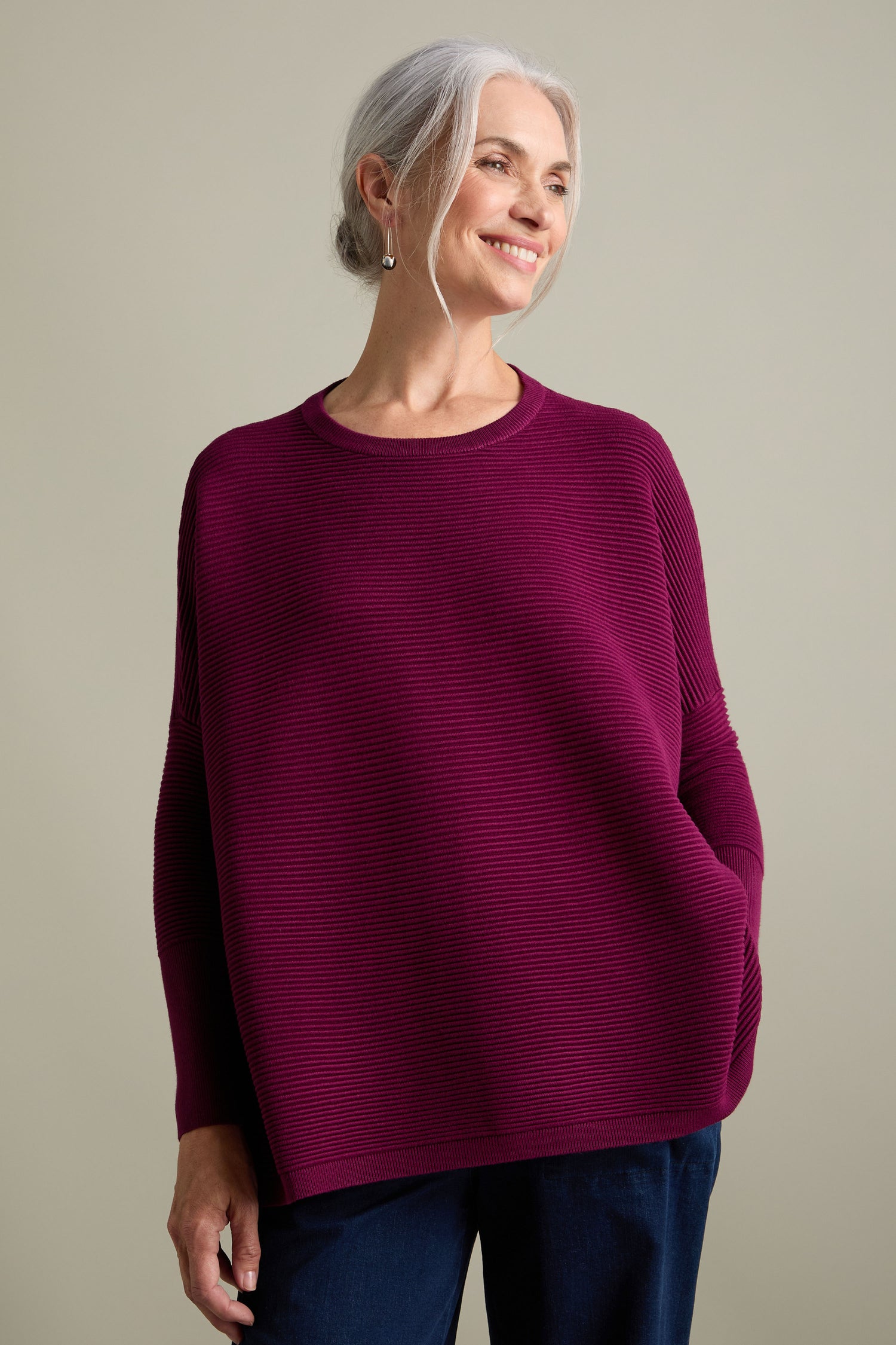 A person with white hair tied back is smiling and wearing a maroon Ribbed Jumper, embracing new-season colors.