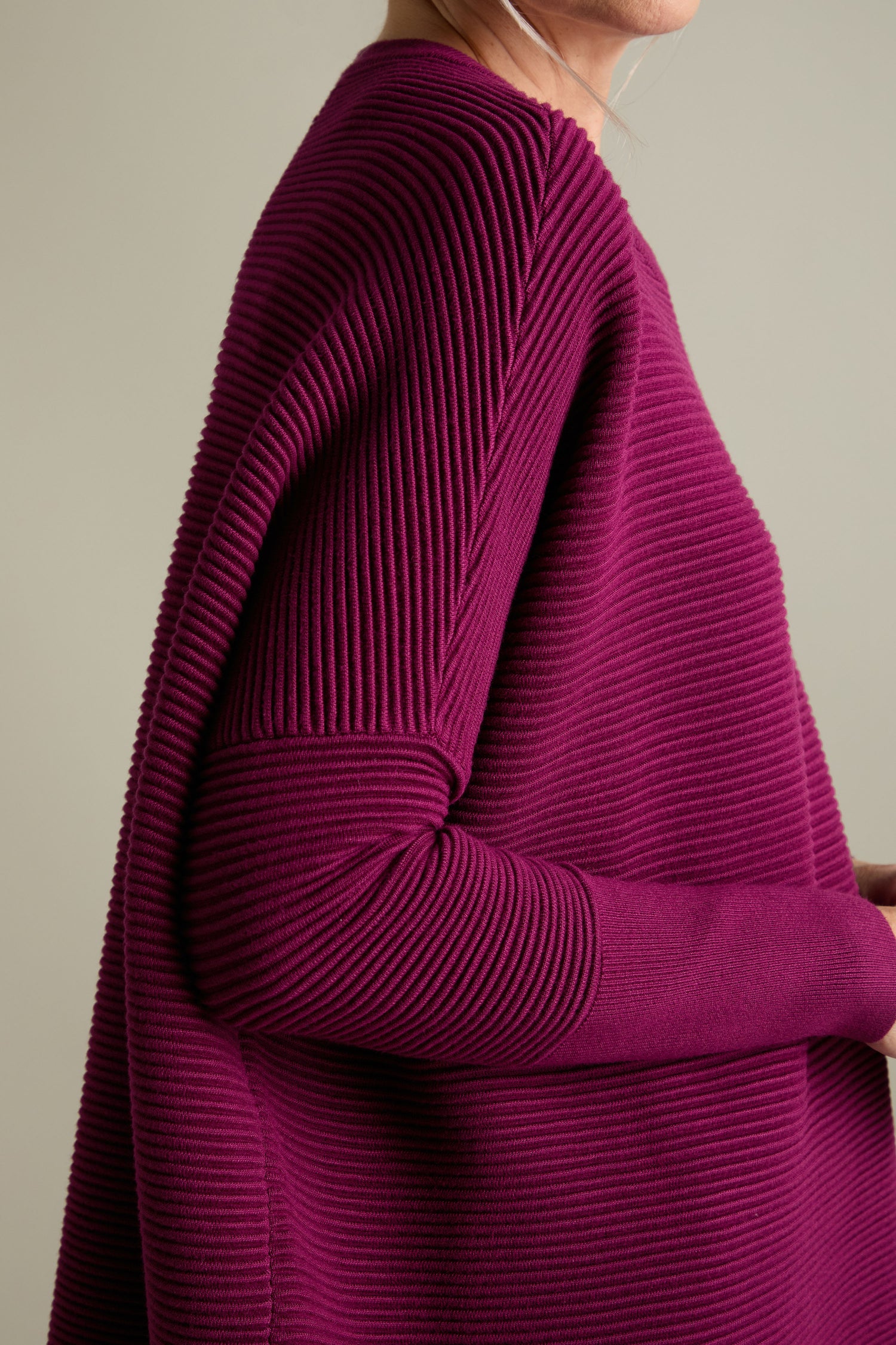 Close-up of a person wearing a Ribbed Jumper in magenta from Paisie. The photo highlights the textured fabric and features the person's upper torso, arm, and partial profile, emphasizing its luxurious feel and one of the new-season colours.