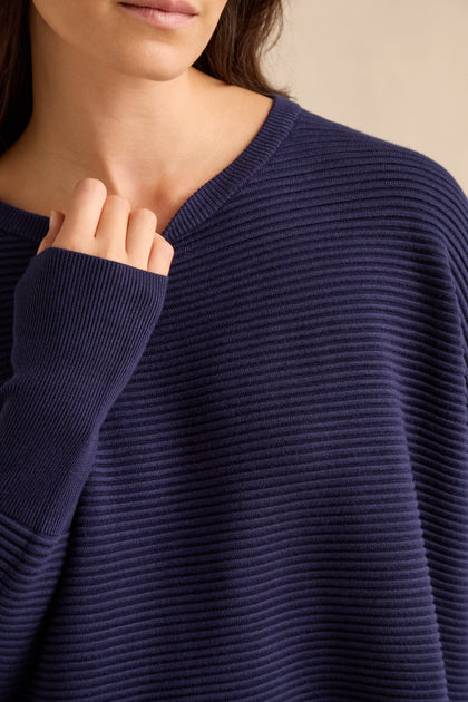 A woman wearing the Navy Ribbed Jumper holds the collar with her left hand. The image is cropped from her nose down to her torso.