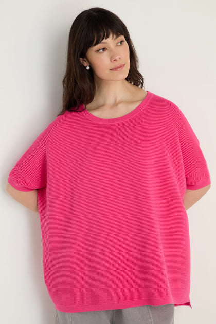 A person with long dark hair wears the Short Sleeve Hot Pink Ribbed Top and light-colored pants, standing against a plain light background.