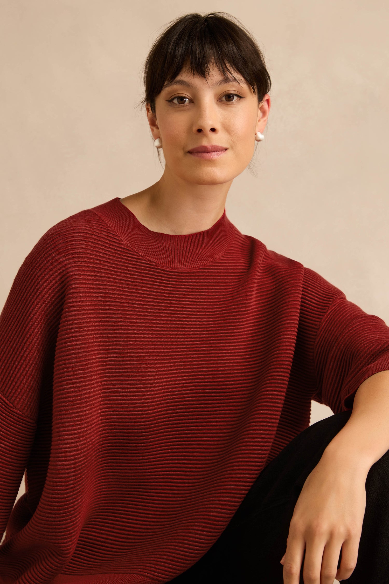 A person with short dark hair wearing the Wide Sleeve Burgundy Ribbed Knit and black pants sits against a neutral background, looking at the camera.