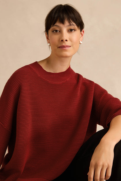 A person with short dark hair wearing the Wide Sleeve Burgundy Ribbed Knit and black pants sits against a neutral background, looking at the camera.