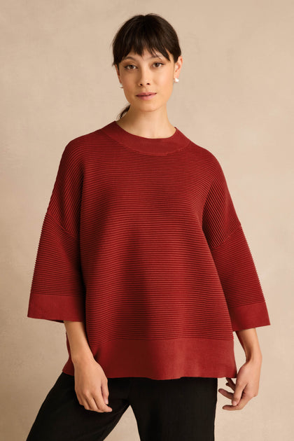 A person stands against a beige background wearing the Wide Sleeve Burgundy Ribbed Knit sweater paired with black pants.
