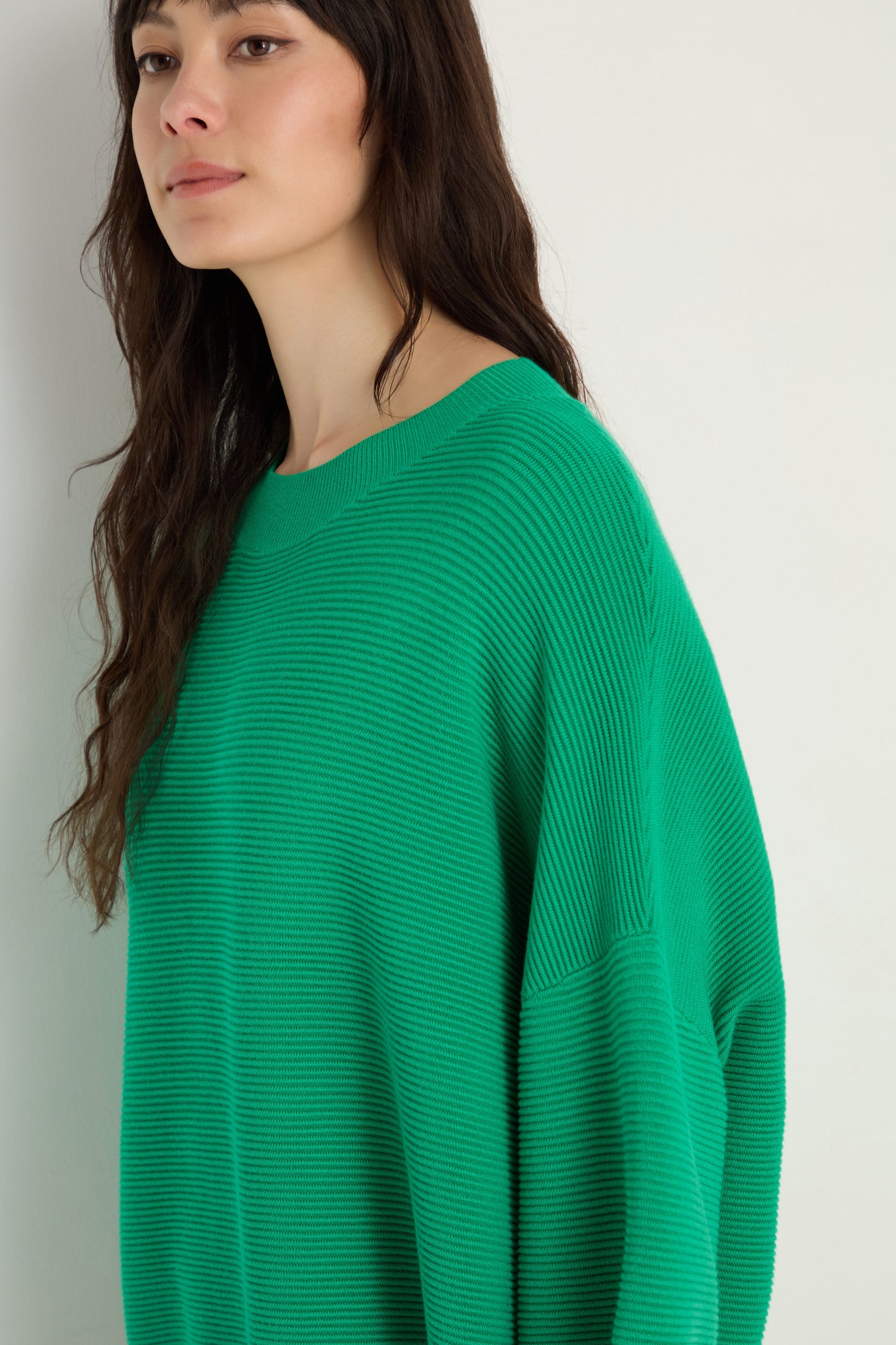 A woman with long dark hair wears the Wide Sleeve Ribbed Top, featuring wide sleeves and a boxy fit. She stands against a light-colored wall, looking slightly to the side.