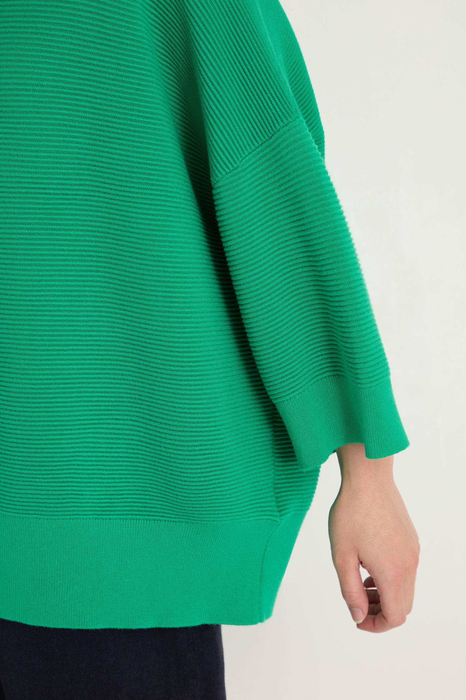 Close-up of a person's arm and hand wearing the Wide Sleeve Ribbed Top, featuring a boxy silhouette in green with three-quarter sleeves and ribbed texture, set against a neutral background.