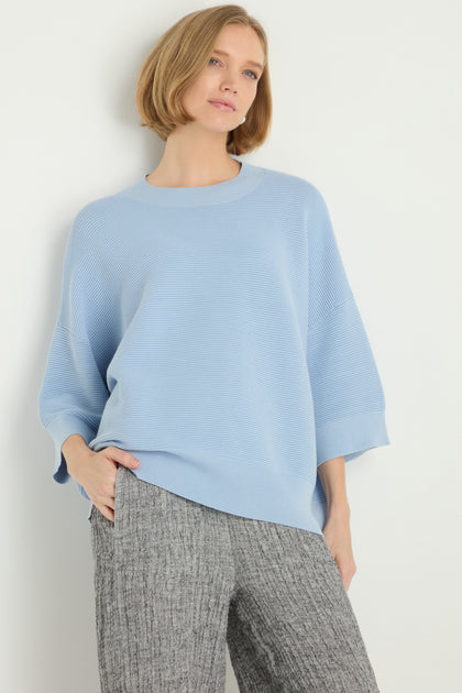 A woman with a short blonde bob models the Wide Sleeve Ribbed Top in light blue and gray textured pants, posing against a plain white background with one hand in her pocket.