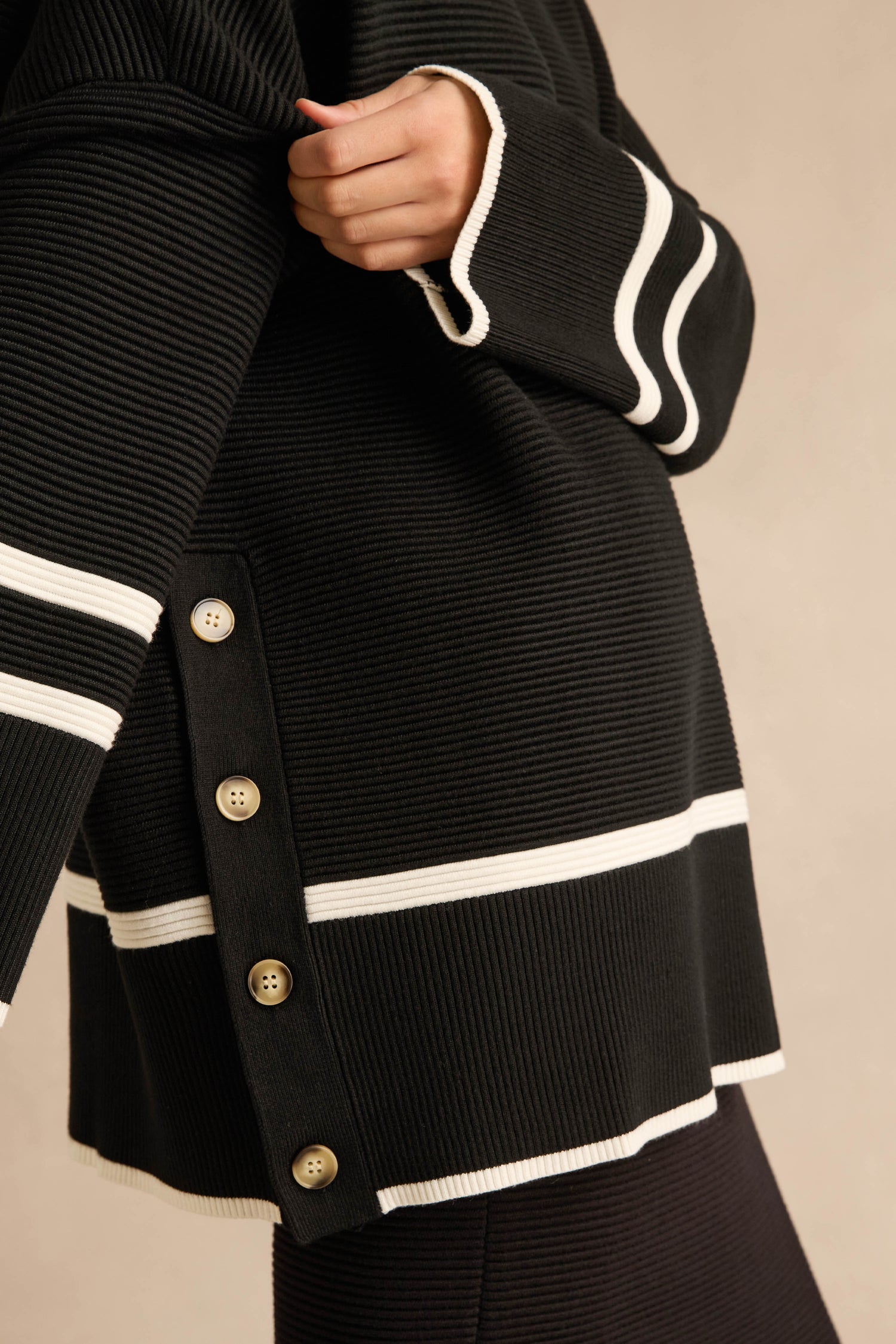 Wearing the Piping Detail Button Ribbed Top, featuring an oversized fit, ribbed texture, white contrast piping, and tan side buttons, the person holds the collar with one hand against a neutral background.
