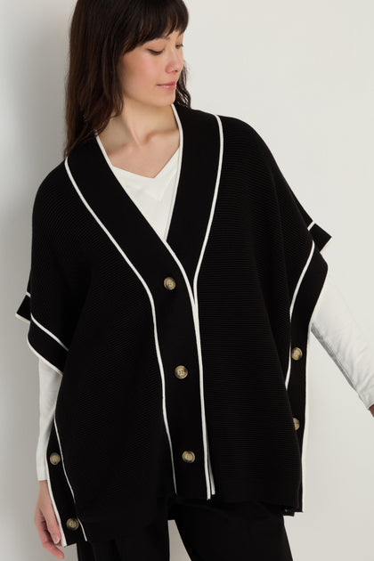 A woman wears the Piped Detail Cardigan, featuring soft viscose blend fabric, white trim, and gold buttons, layered over a white top against a plain light background.