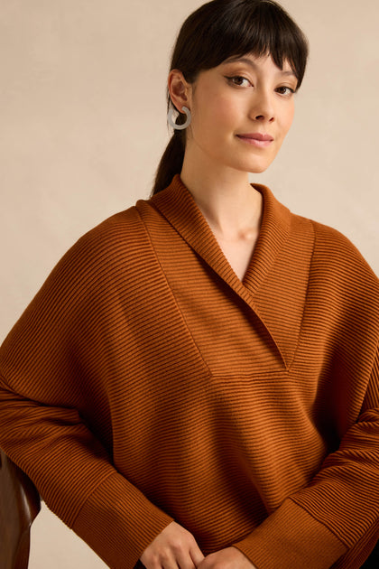 Woman with dark hair in a ponytail wearing the Shawl Collar Copper Ribbed Knit sweater and silver hoop earrings, looking at the camera against a neutral background.