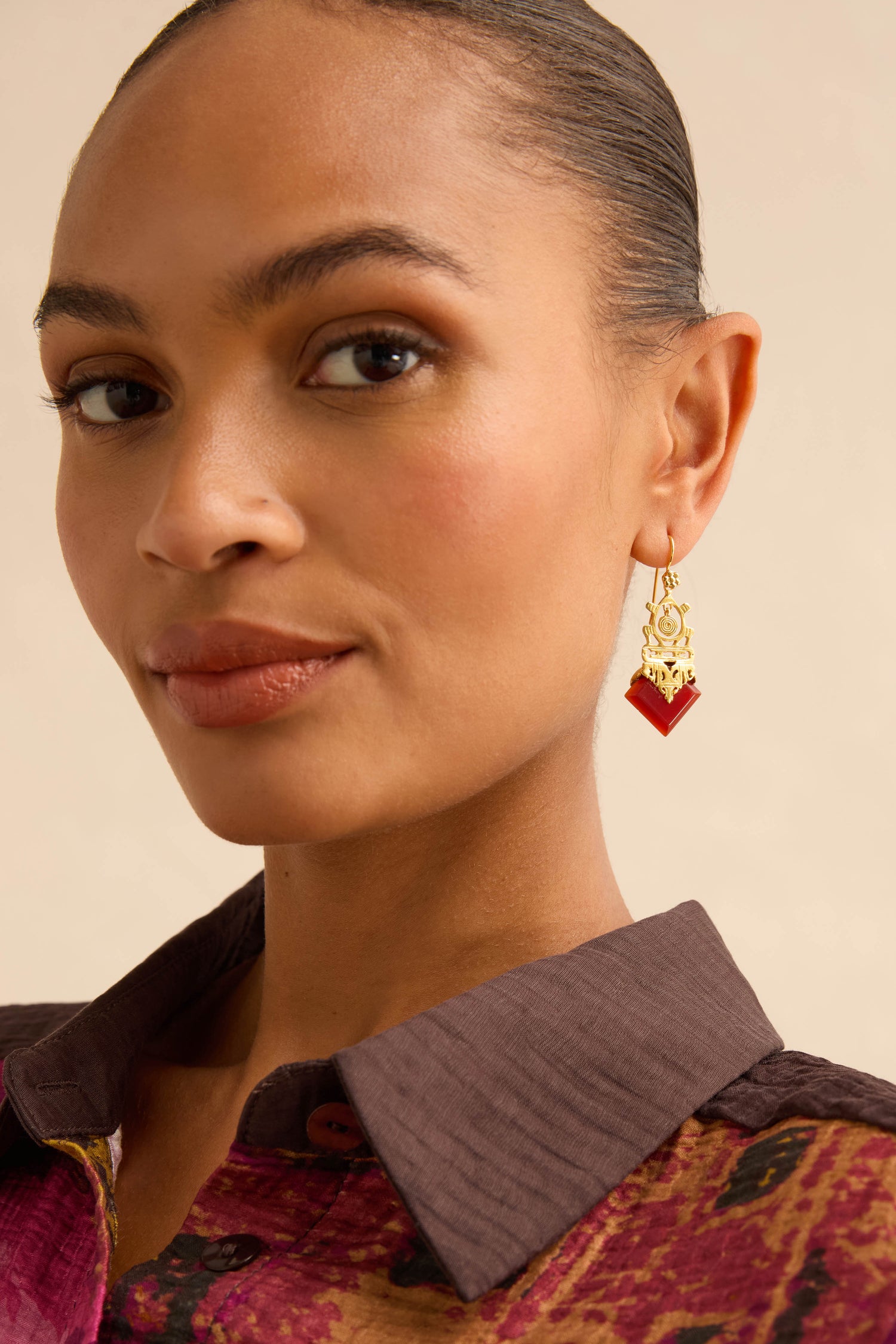 A woman wearing Gold-Plated Carnelian Drop Earrings, featuring a geometric design with a diamond-shaped red stone.