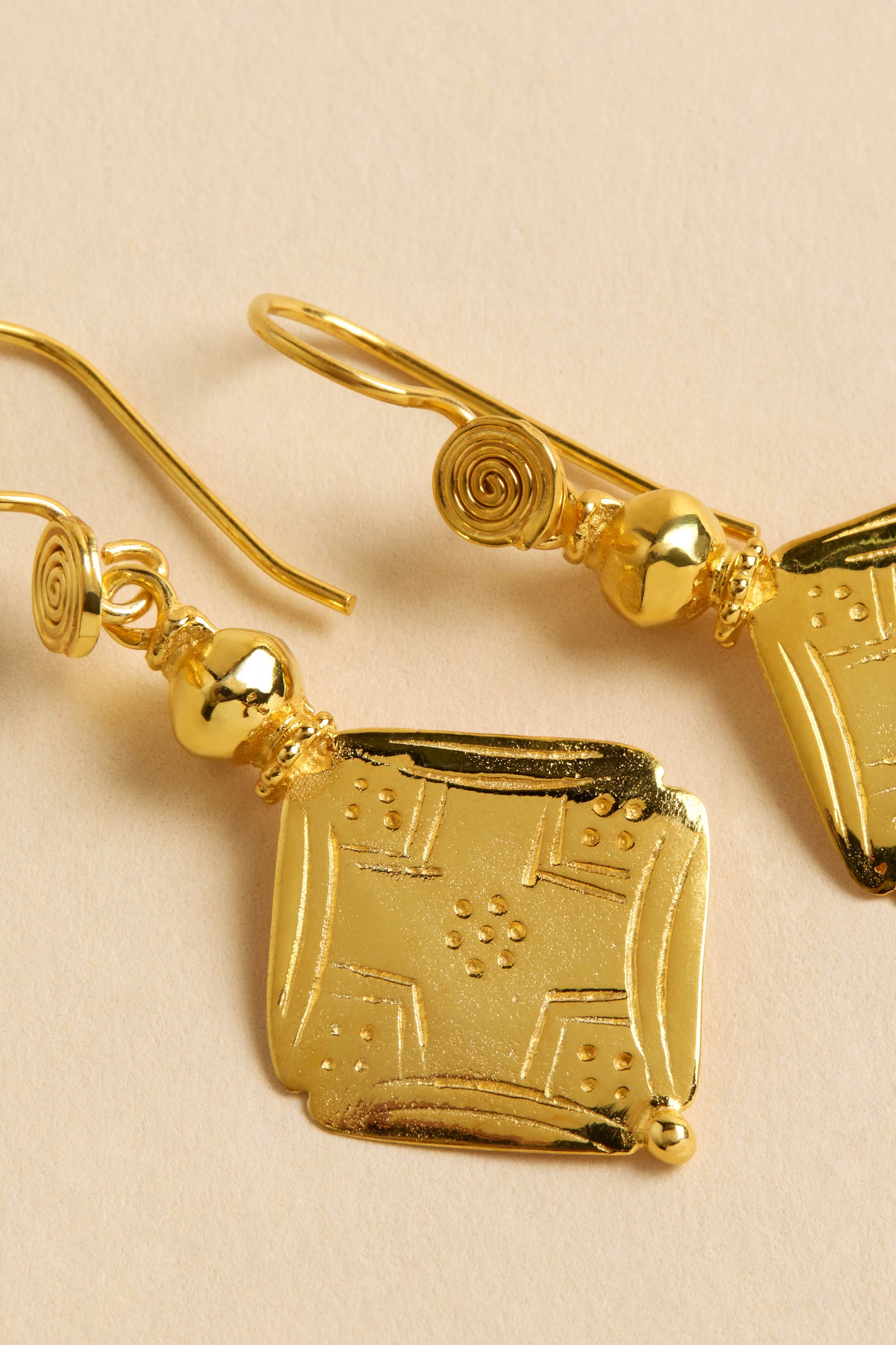 Close-up of Gold-Plated Square Drop Earrings with engraved square pendants, round beads, and spiral hooks on a neutral background.
