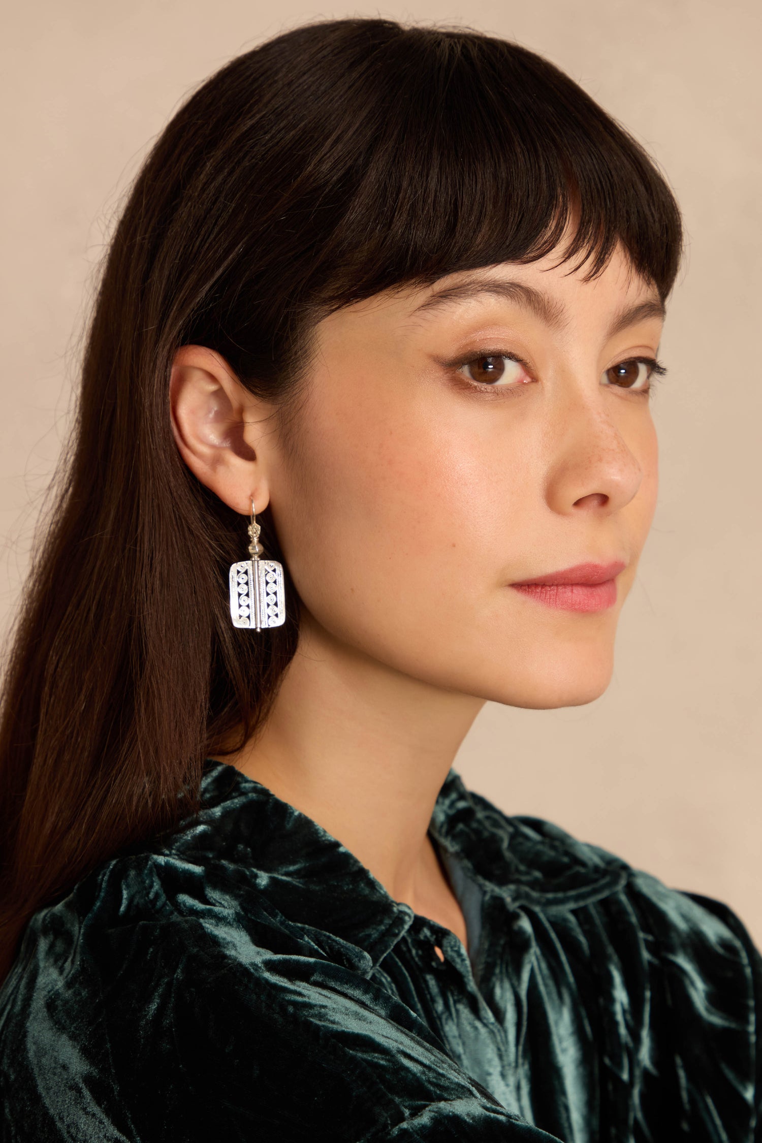 Woman with straight dark hair in a green velvet top wears Filigree Drop Earrings, looking to the side against a neutral background.