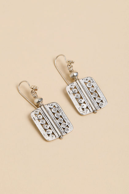 Filigree Drop Earrings—rectangular silver drops with swirl and line details, small round accents, and hooks, shown on a beige background.
