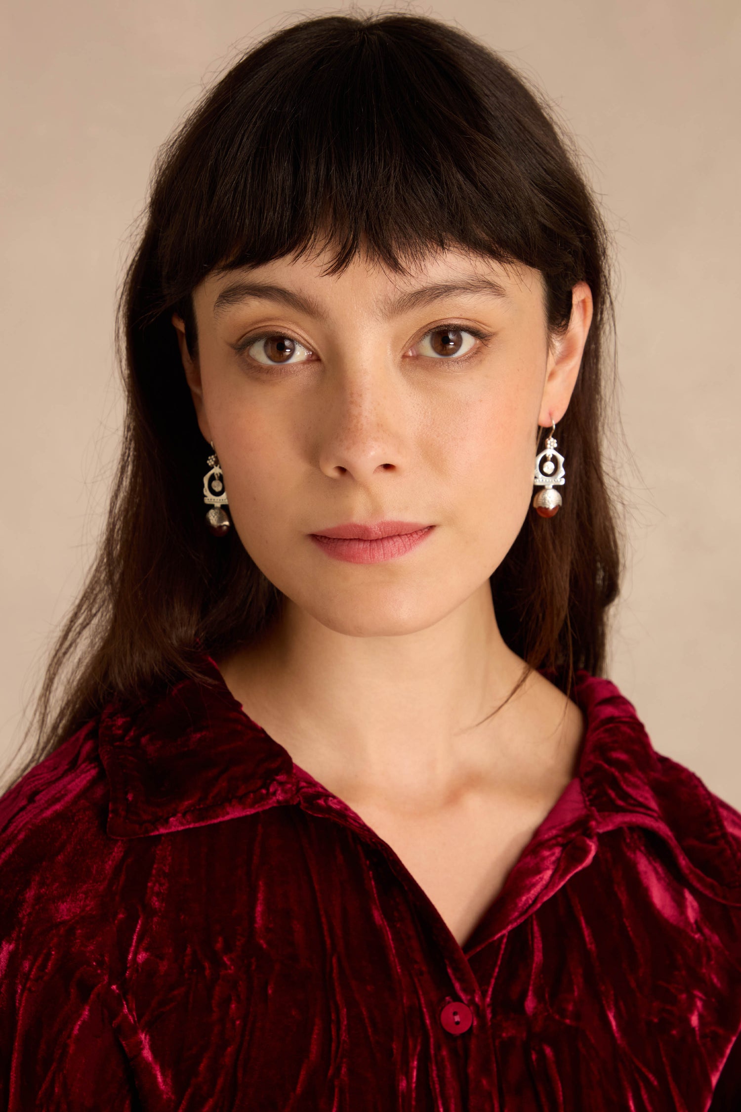 Woman with long dark hair, wearing a red velvet shirt and the Carnelian Drop Earrings, looks directly at the camera against a neutral background.