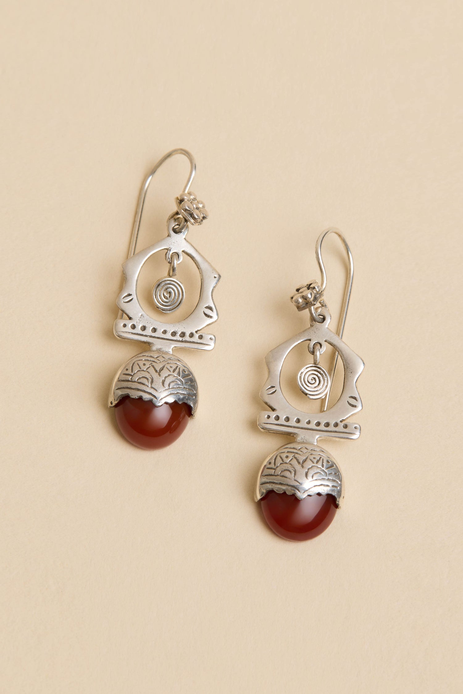 Carnelian Drop Earrings: Sterling silver geometric drops with spiral details and red carnelian stones, shown on a light beige background.