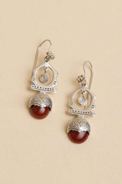 Carnelian Drop Earrings: Sterling silver geometric drops with spiral details and red carnelian stones, shown on a light beige background.