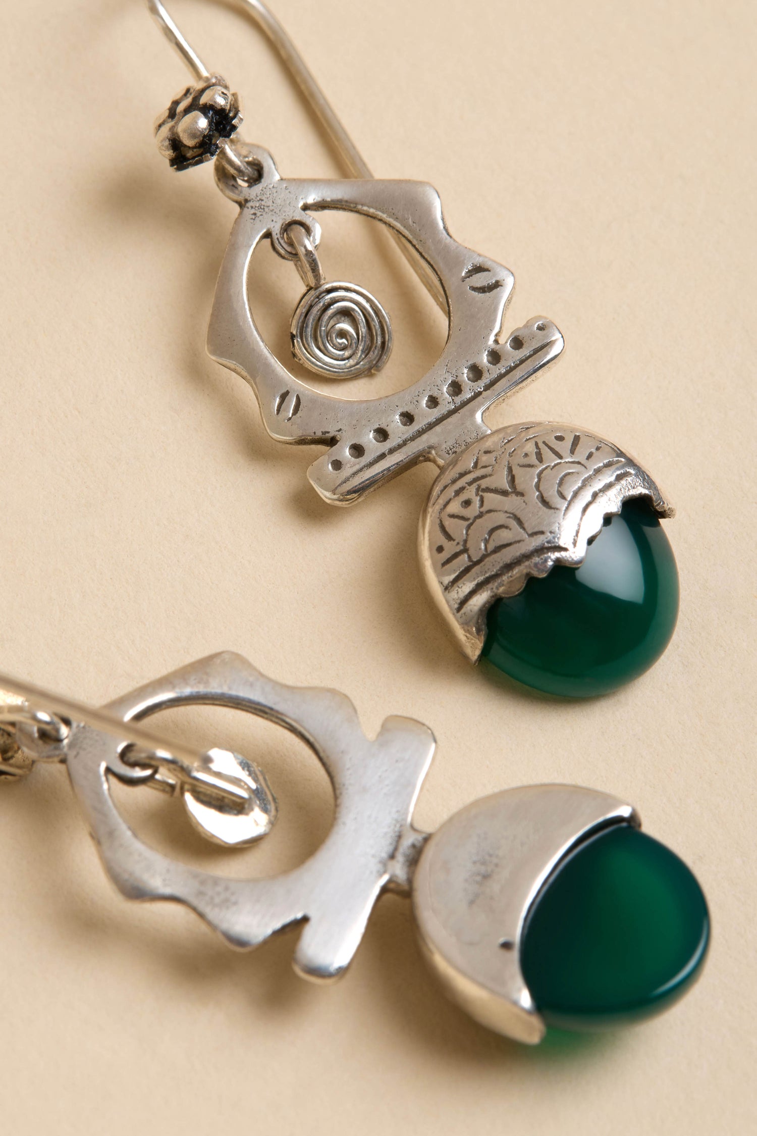 Close-up of Green Onyx Drop Earrings in sterling silver with intricate engraved and cut-out designs, laid on a neutral beige surface.