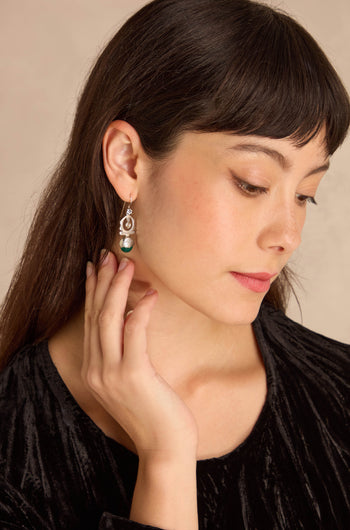A woman with long dark hair touches her Green Onyx Drop Earrings set in sterling silver. She has natural nails and a small tattoo on her wrist.