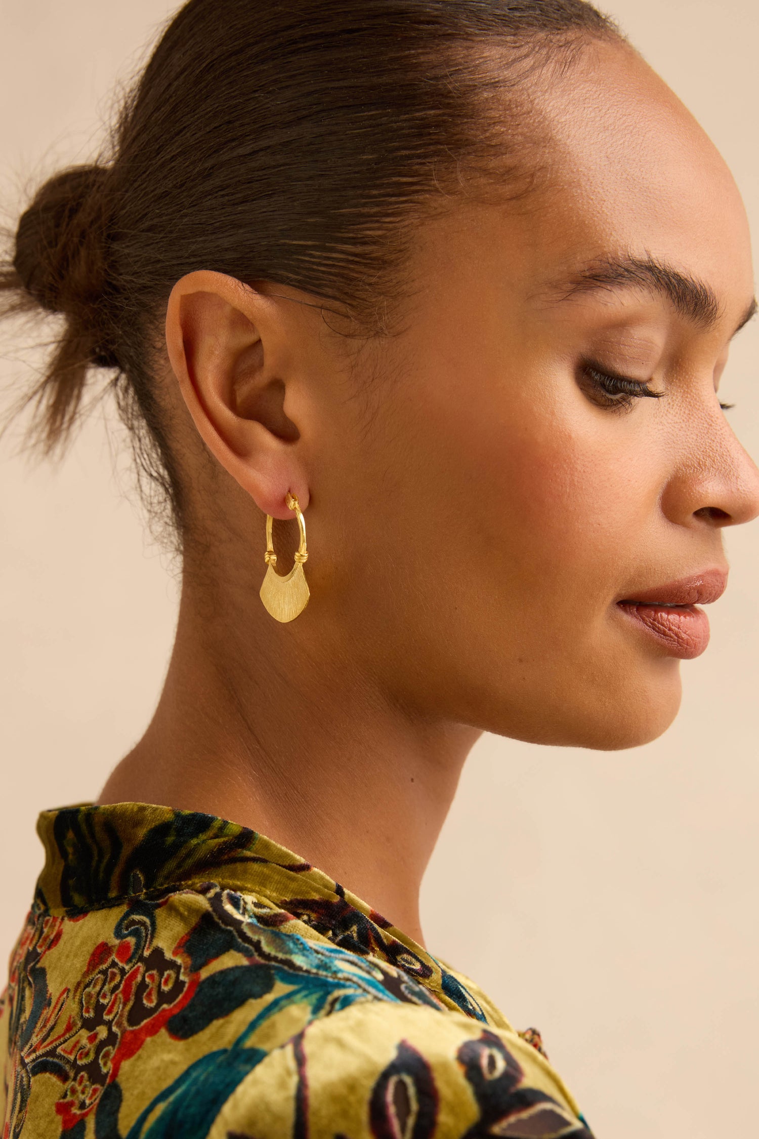 Gold-Plated Fan Hoop Earrings featuring a flat, fan-shaped charm with a linear textured finish, worn by a woman in profile.