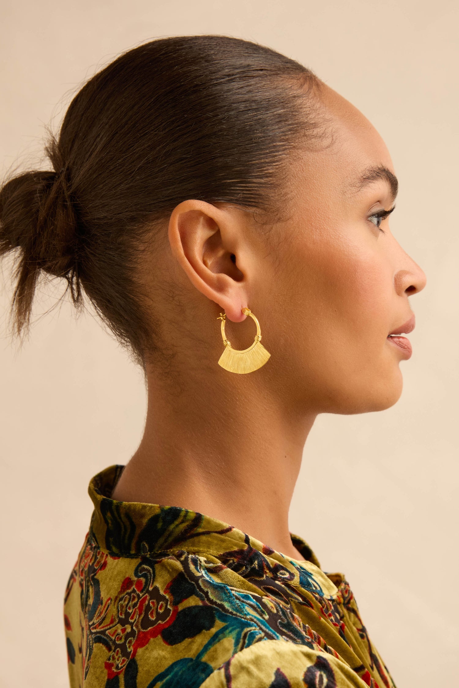 Profile view of a person wearing a Gold-Plated Fan Hoop Earring featuring a pleated, fan-shaped charm with a linear textured finish.