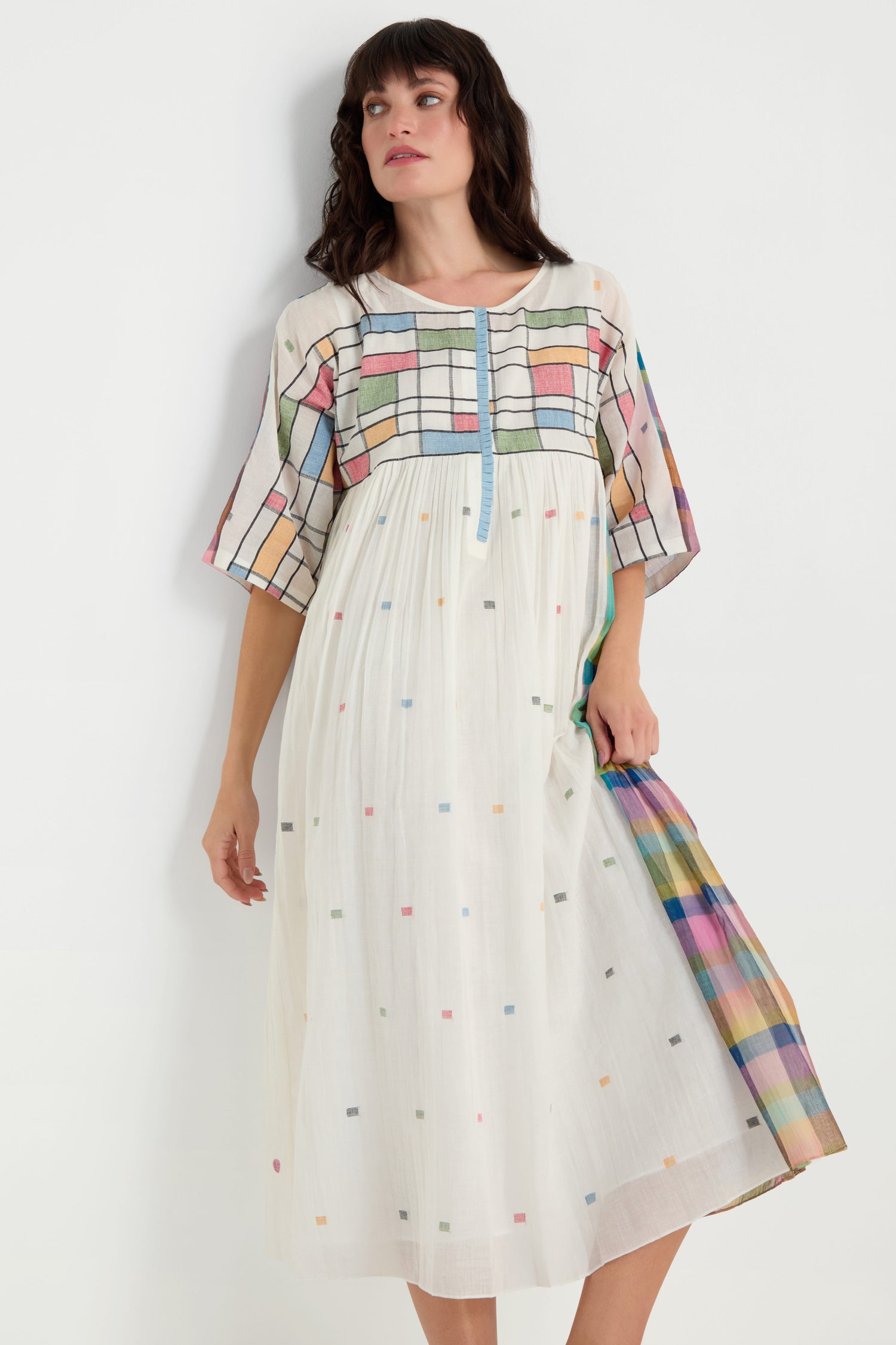 Woman wearing the Mondrian Jamdani Dress, made from cotton and featuring colorful geometric patterns on the bodice, sleeves, and hem, standing against a plain white background.