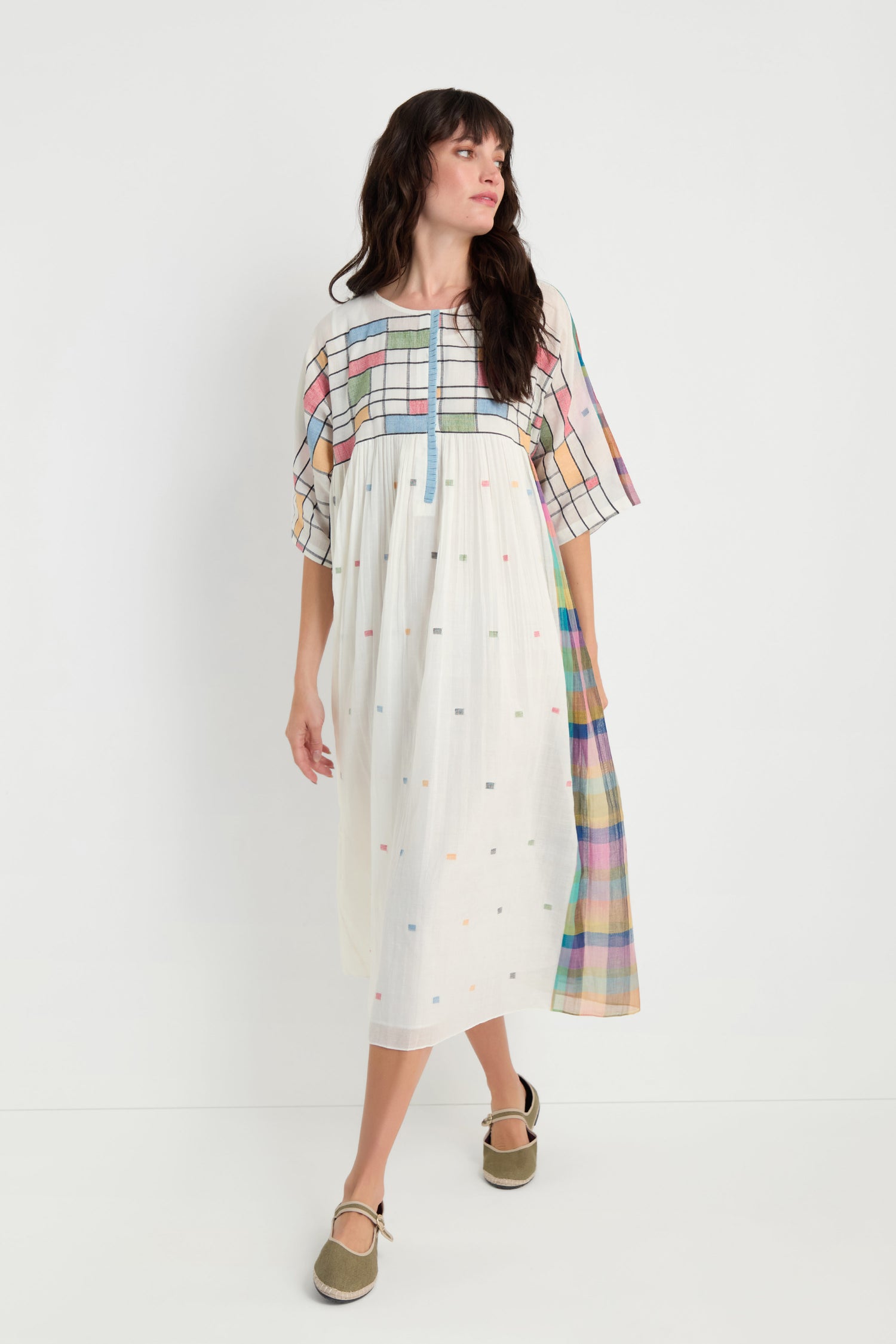A woman models the Mondrian Jamdani Dress—a loose, knee-length cotton dress with pastel plaid and polka dot patterns—standing against a plain white background.