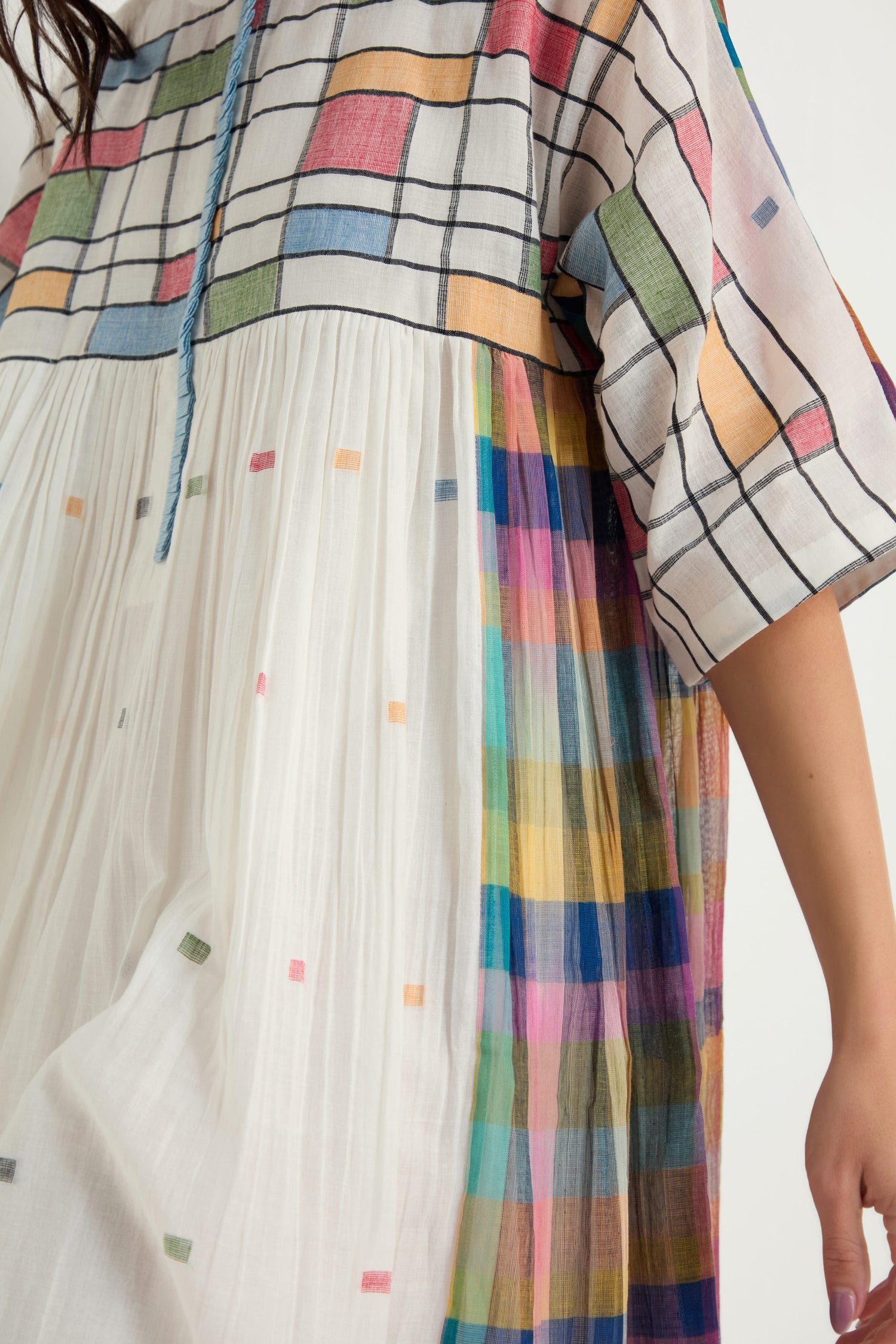 Wearing the Mondrian Jamdani Dress—white and loose-fitting, it features colorful grid and square patterns on the top, sleeves, and sides, plus small colored squares inspired by traditional jamdani weaving.