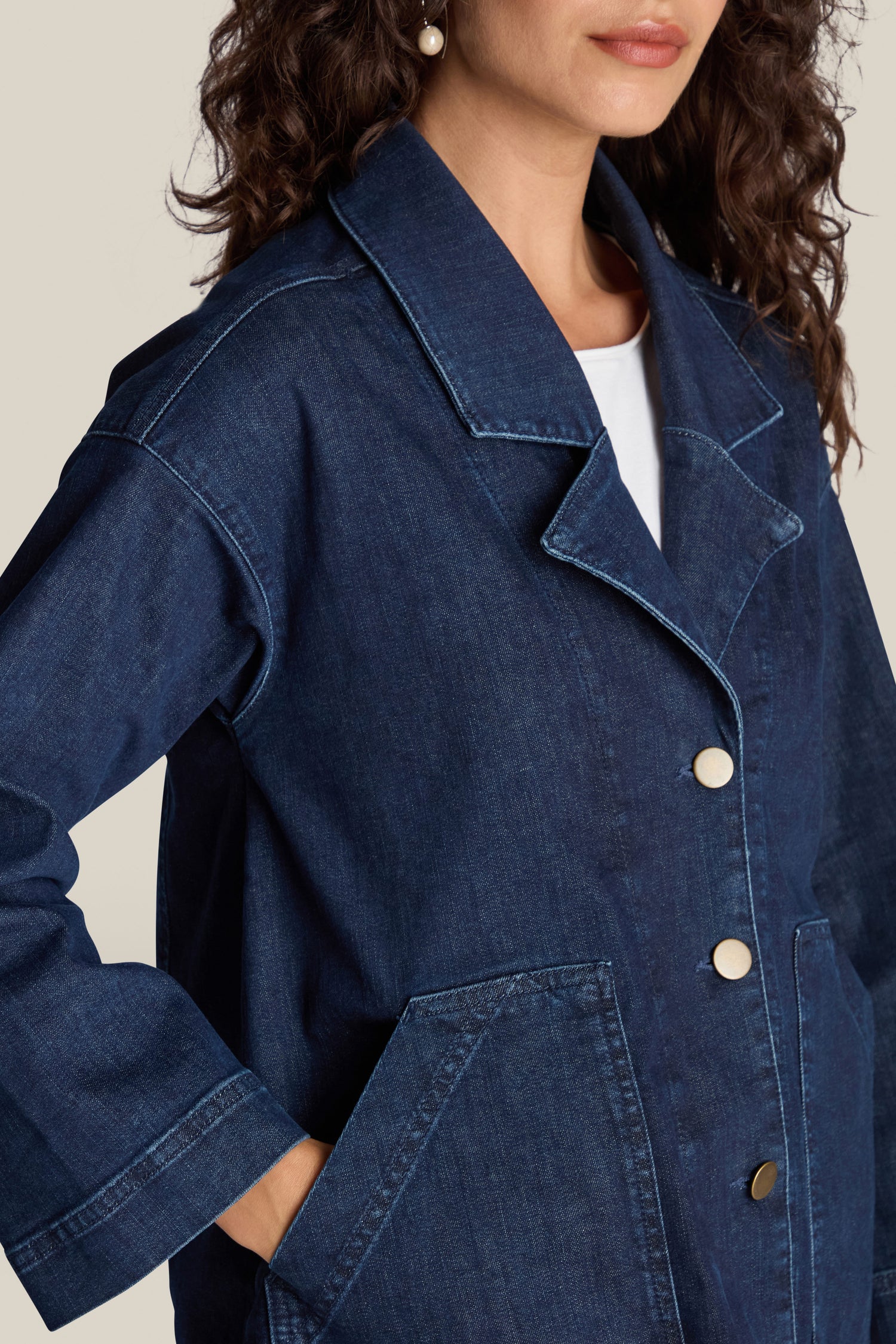 A person with curly hair wears a Stretch Denim Jacket in dark blue, featuring large front pockets, gold-toned buttons, and a contemporary fit.