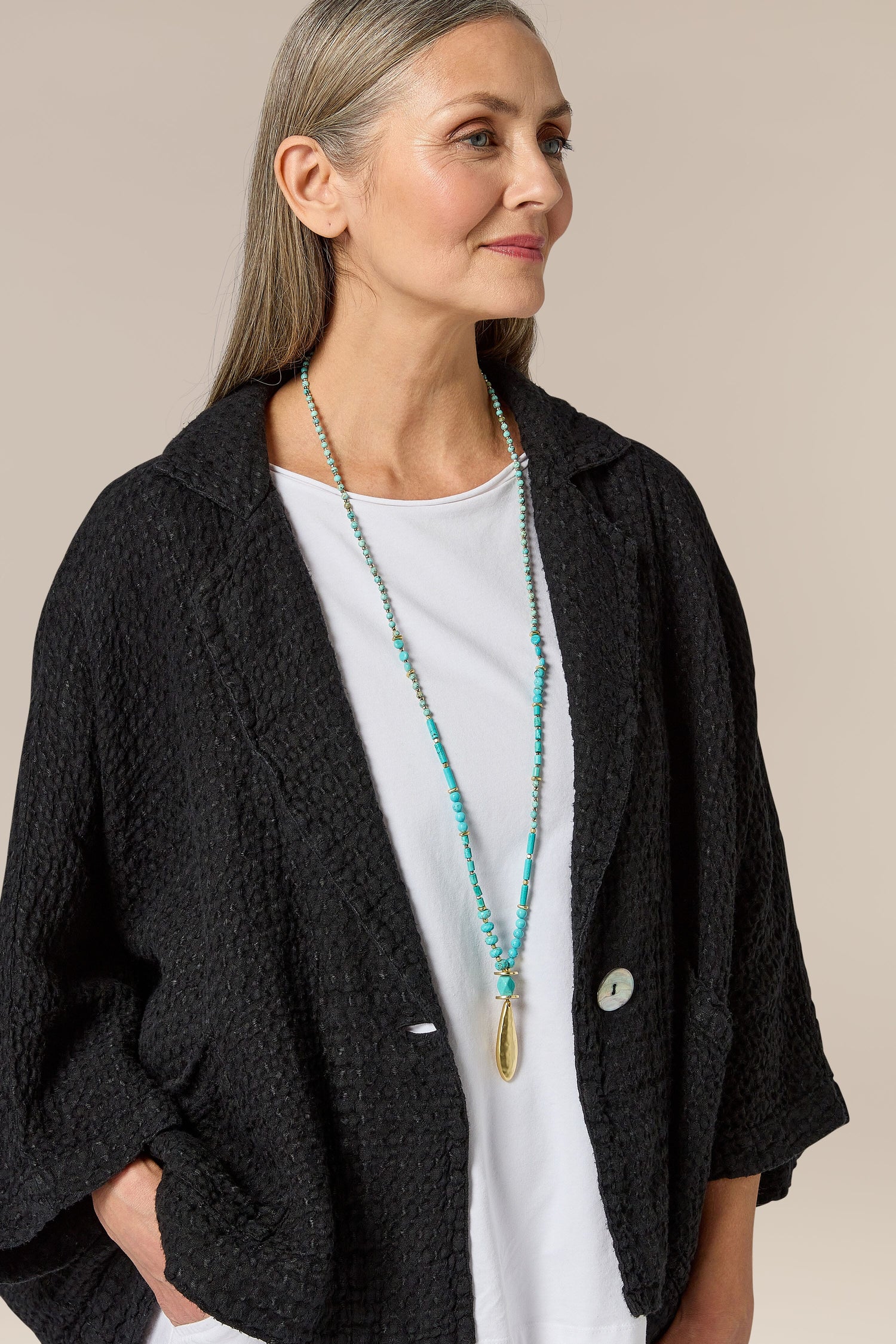 A woman wearing a black jacket and [Turquoise Bead Gold Pendant], adding a touch of bohemian flair to her outfit.