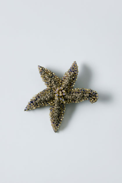 The Hand Beaded Starfish Brooch features decorative texture, crystal beads, and metallic accents, elegantly displayed on a plain light background.