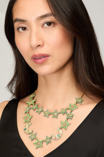 A woman in a black top wears the Hand Beaded Celestial Necklace, featuring green star and crescent moon shapes with sparkling embellishments.