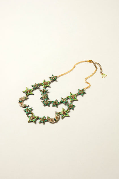 The Hand Beaded Celestial Necklace features double strands with green star and crescent moon pendants adorned with colorful stones, shown on a neutral background—a beautifully handcrafted jewelry piece.