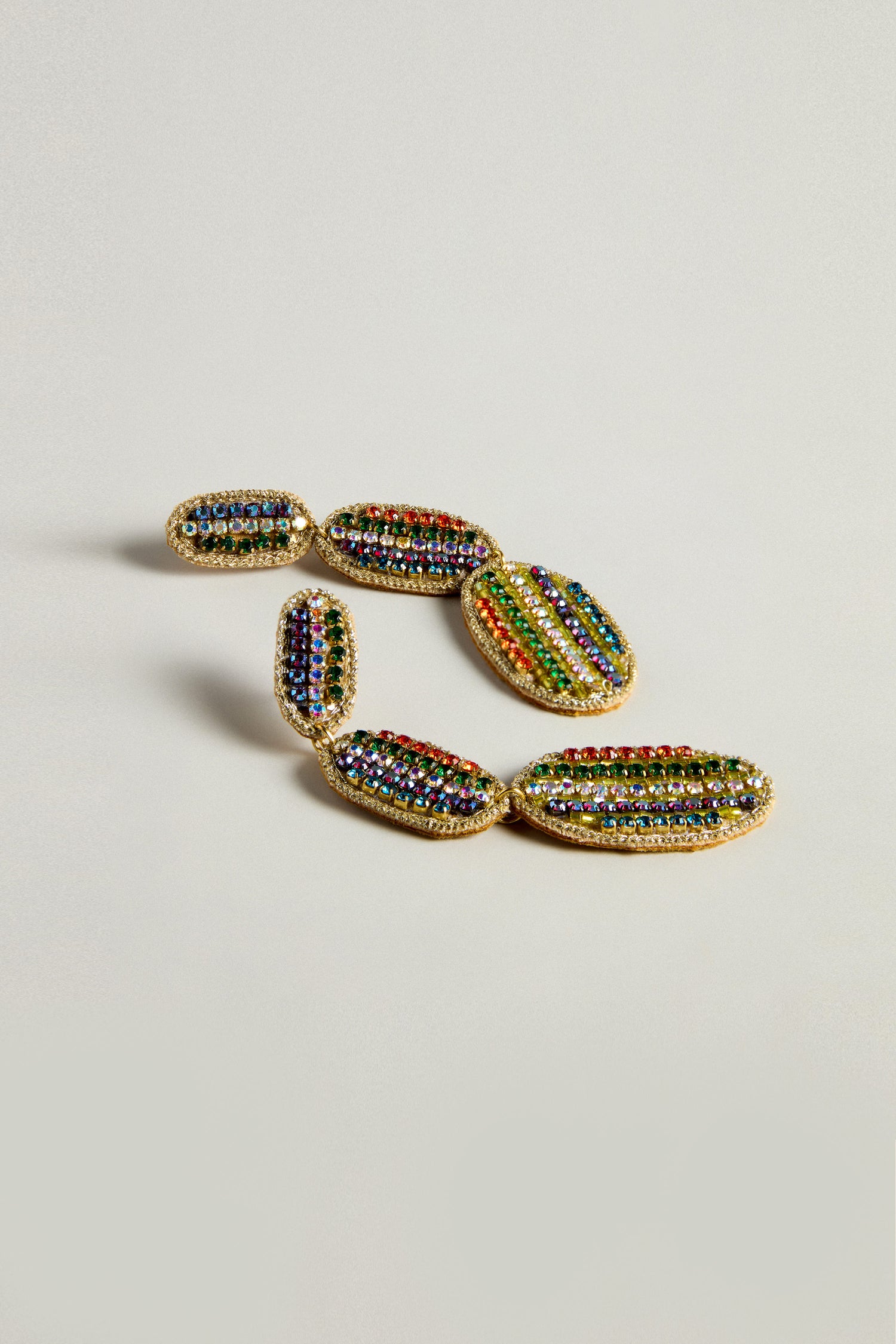 A pair of Hand Embroidered Crystal Bead Earrings features a vibrant drop design with gemstone-encrusted oval links, arranged in a curved pattern on a light background.