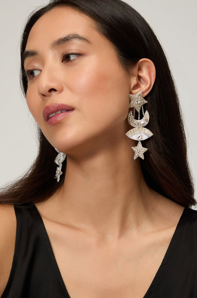 Woman with long dark hair wearing Psquuare Fashion Jewellery's Hand Beaded Celestial Silver Earrings, featuring star and crescent designs, paired with a sleeveless black top for a striking, modern look.