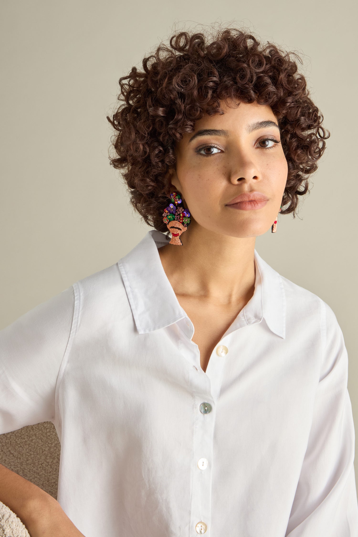 A person with curly hair wears a white shirt and vibrant Hand Beaded Frida Earrings, sitting against a neutral background.