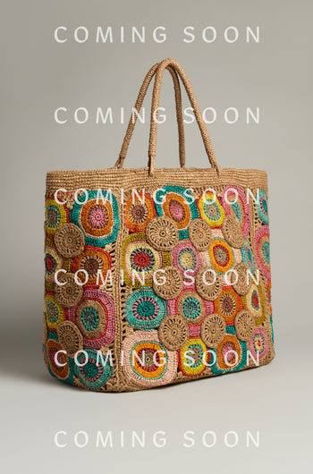 The vivid Handwoven Circles Raffia Bag, featuring circular designs and dual handles, pops against a simple background. Text reads "COMING SOON.