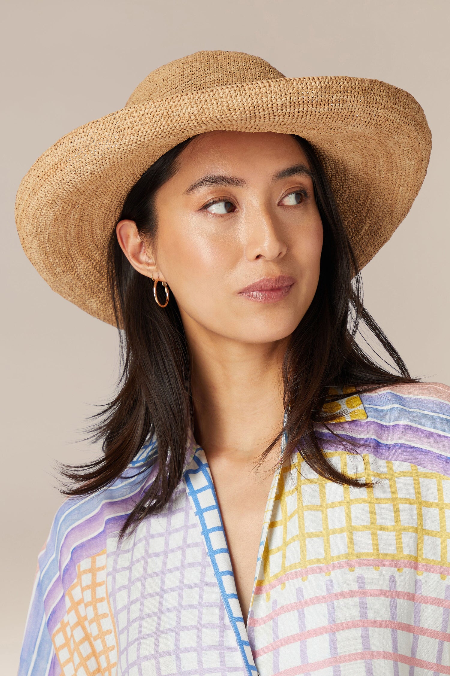 Woman wearing a Madagascar Wide Brim Woven Raffia Hat and colorful blouse looking to the side.