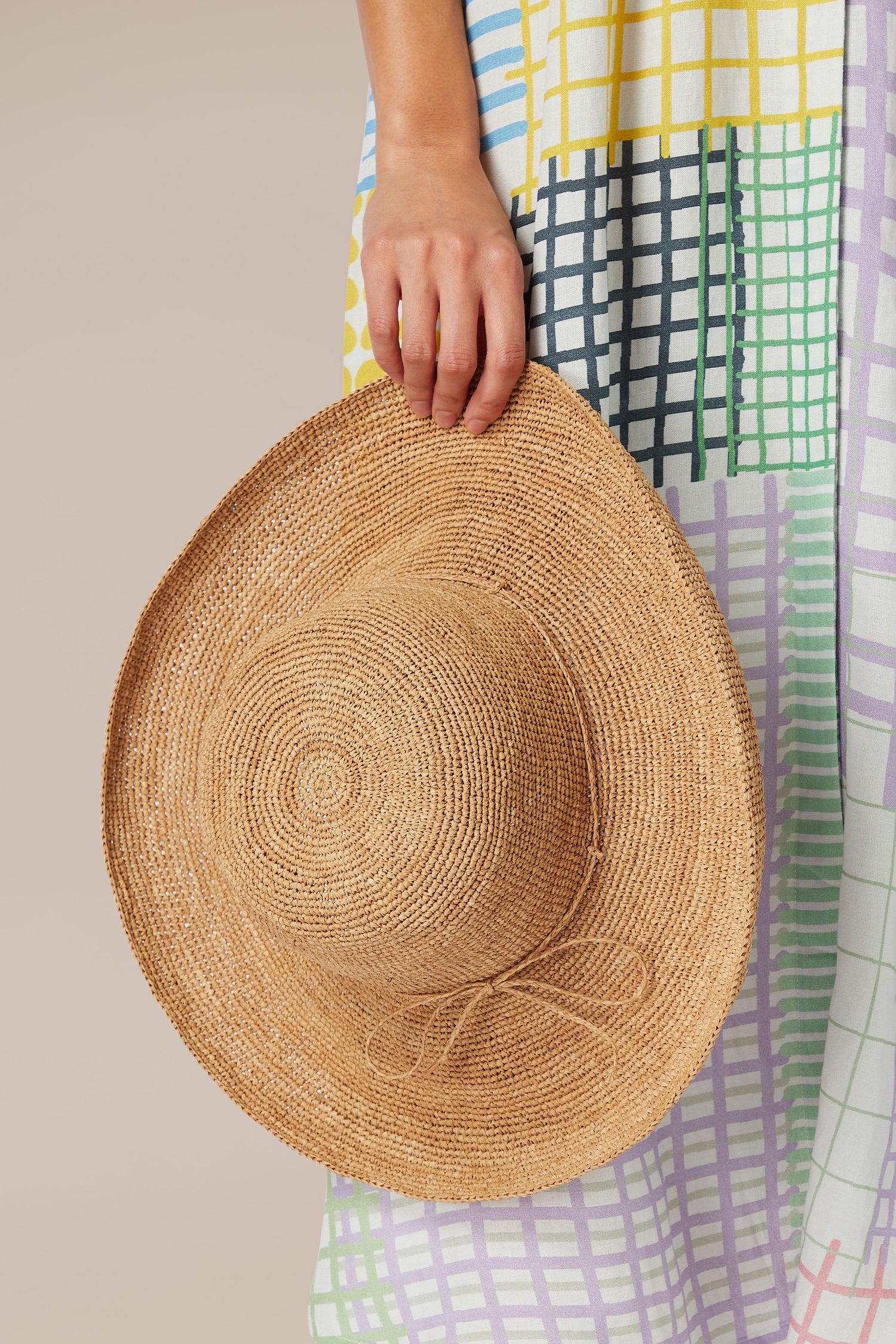 A person holding a Wide Brim Woven Raffia Hat against a Rabarany patterned dress.