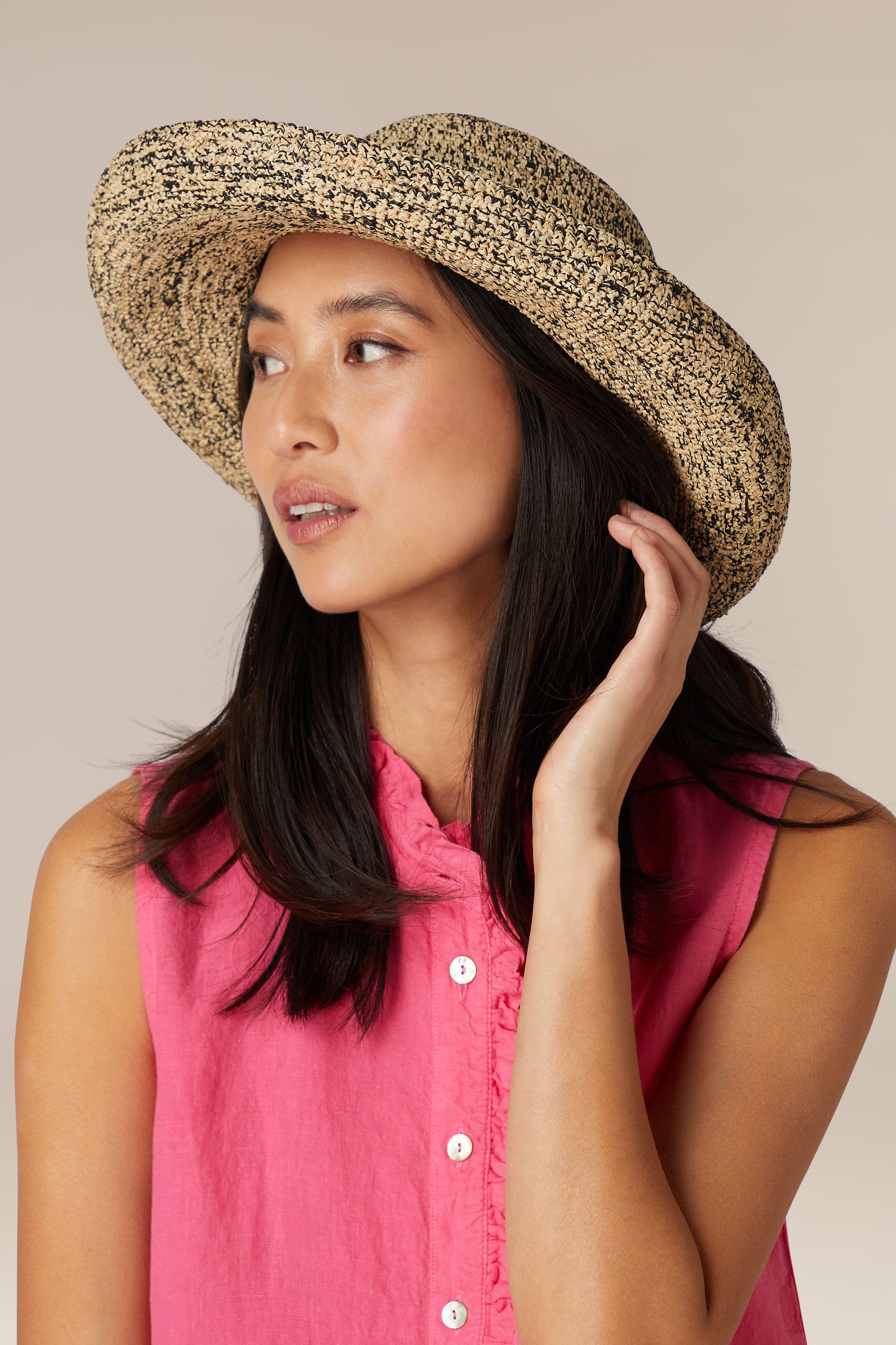 A woman in a pink sleeveless shirt and a Wide Brim Woven Raffia Hat, looking to the side in Madagascar.