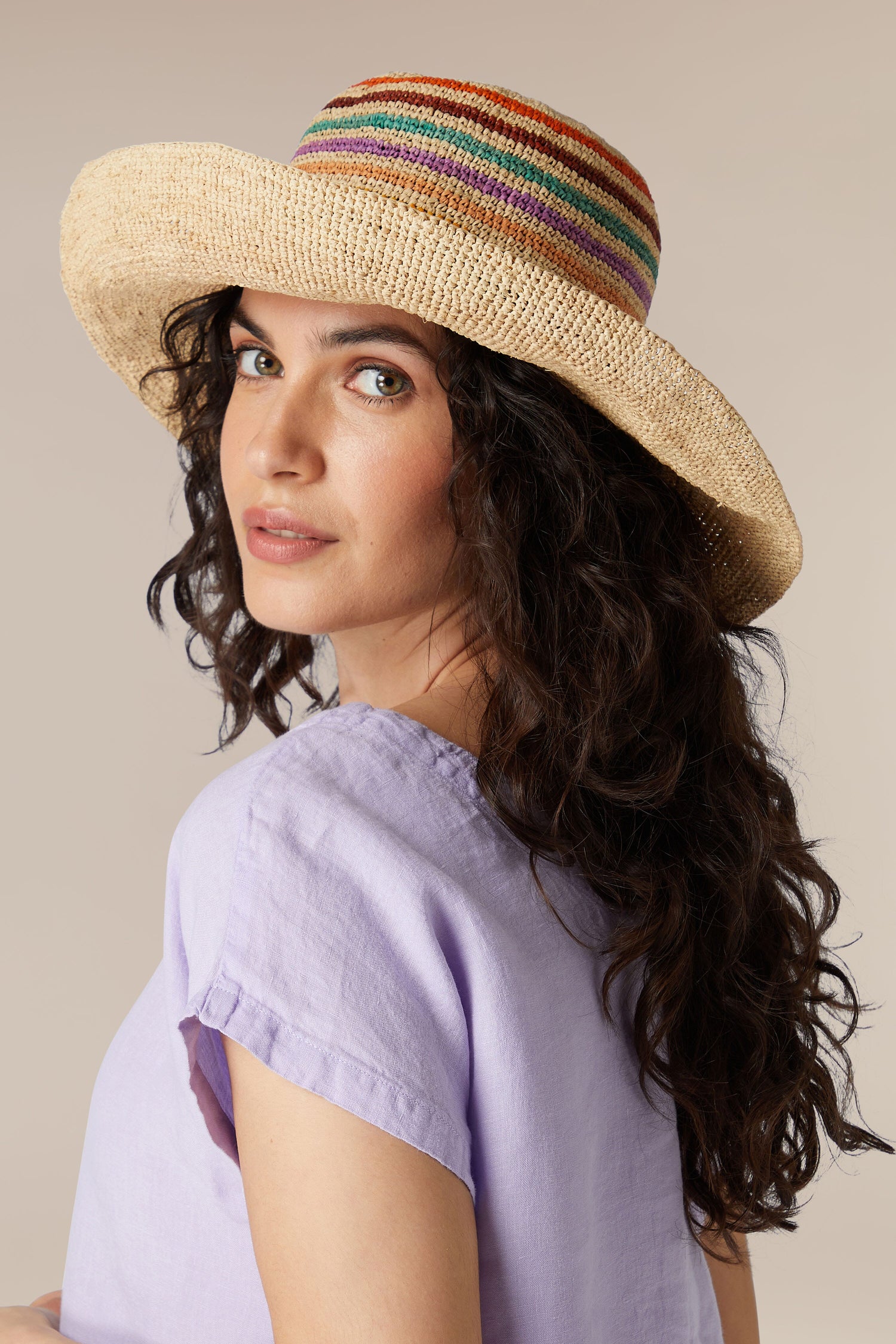 A woman with curly hair wearing a Wide Brim Woven Raffia Hat with a colorful band, looking over her shoulder in Madagascar.