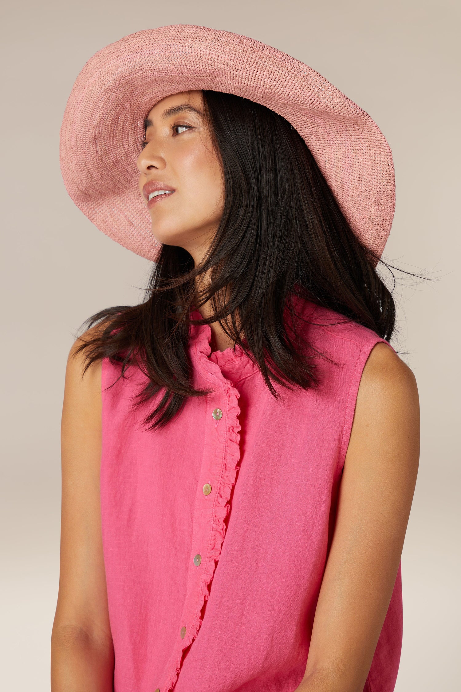 Woman in a pink outfit and Wide Brim Woven Raffia Hat looking to the side.