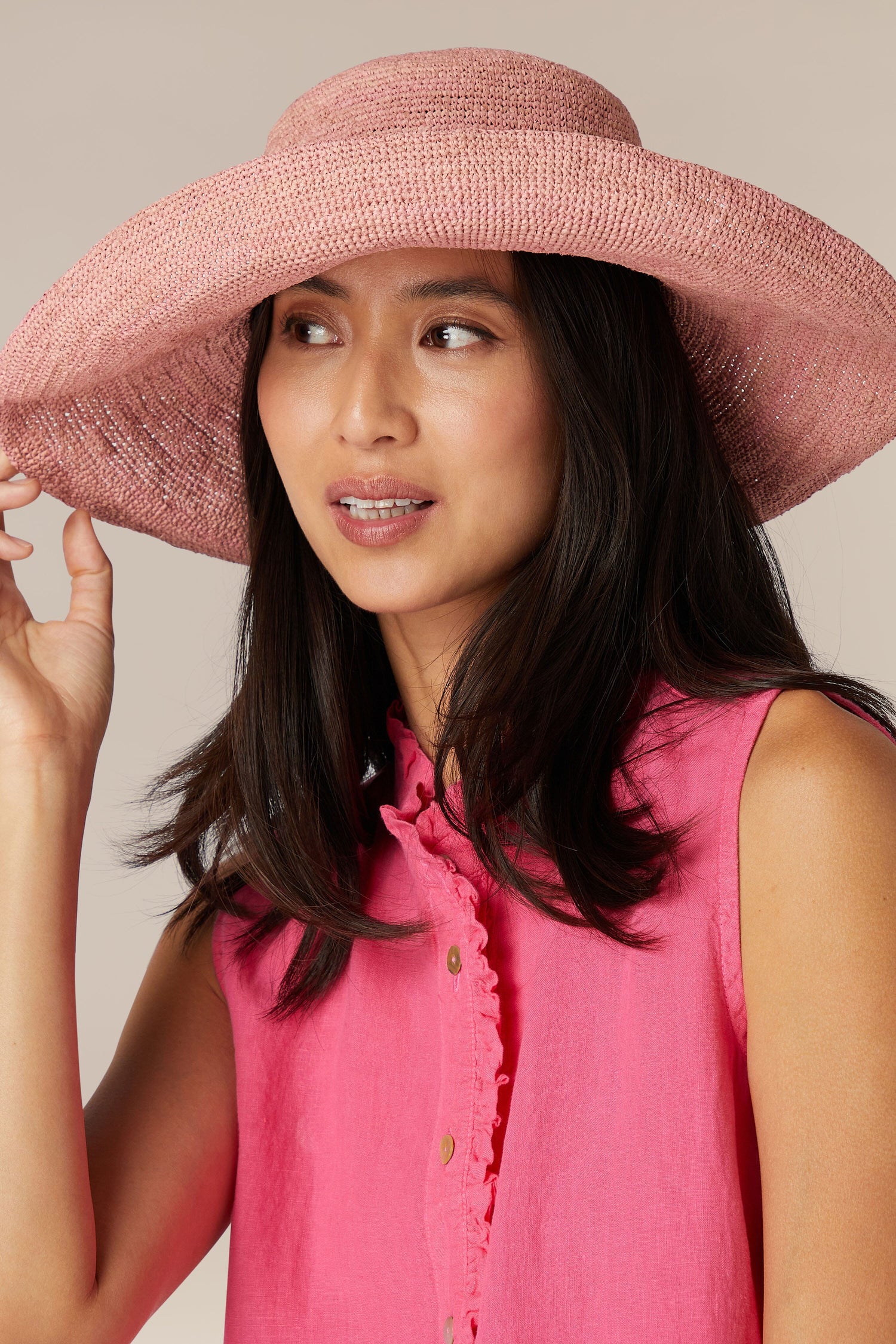 Woman wearing a The Emily wide brim woven raffia hat and sleeveless blouse looking to the side in Rabarany, Madagascar.