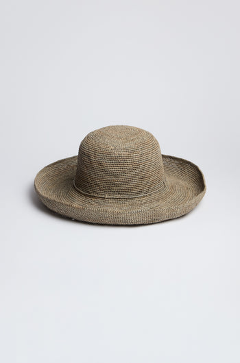 The Handwoven Wide Brim Raffia Hat features a rounded crown and sits elegantly on a plain, light gray background, providing stylish sun protection.