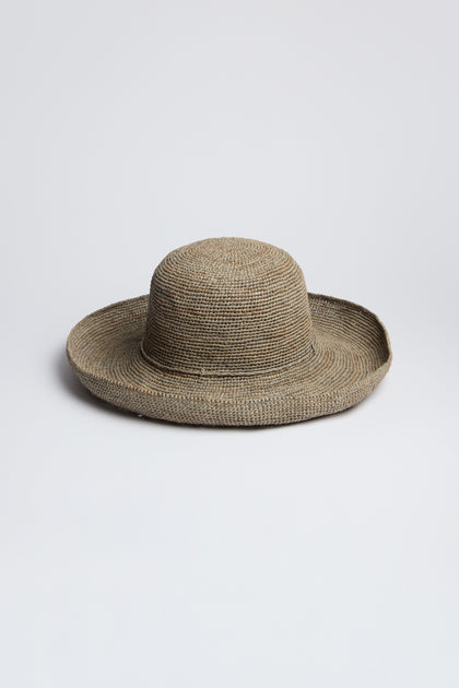 The Handwoven Wide Brim Raffia Hat features a rounded crown and sits elegantly on a plain, light gray background, providing stylish sun protection.