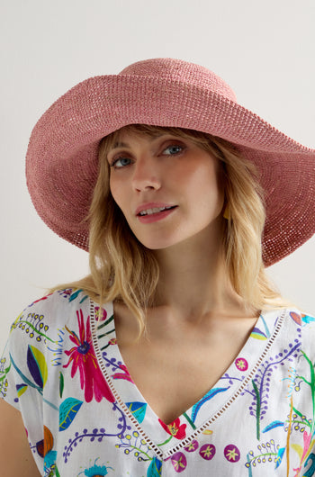 A person in a floral blouse wears a Handwoven Wide Brim Raffia Hat, standing against a plain background.
