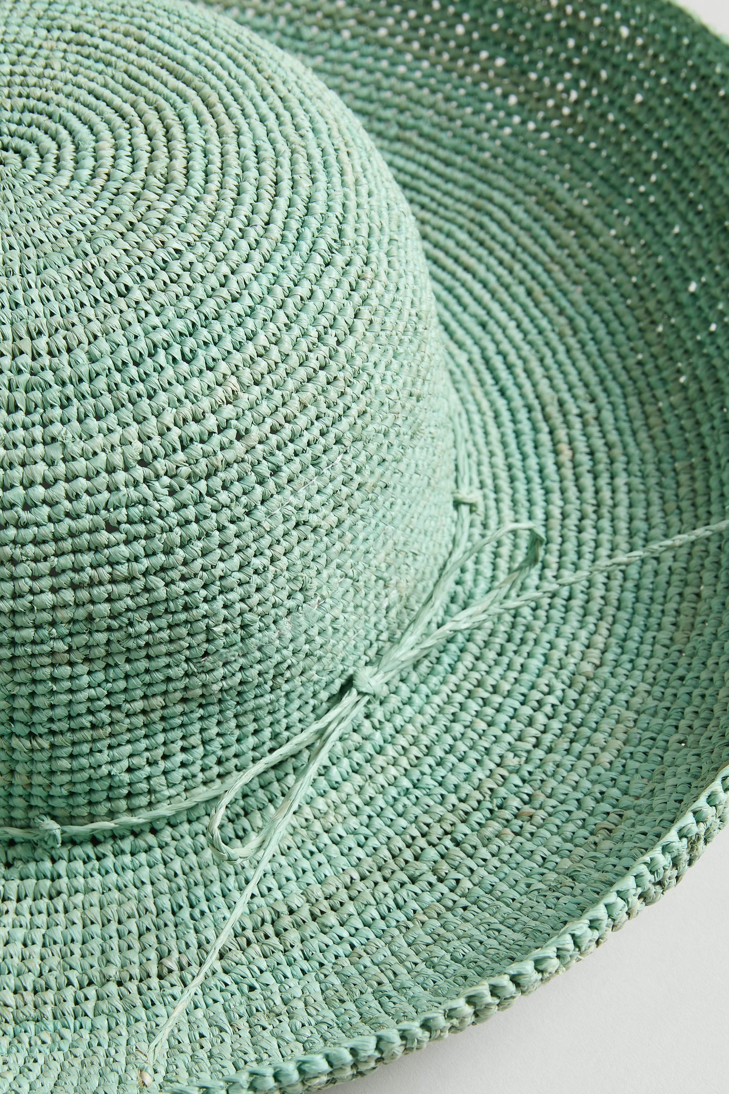 Close-up of the Handwoven Wide Brim Raffia Hat in light green, crafted in Madagascar and featuring a thin decorative bow.